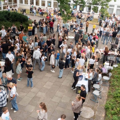 Viele Menschen besuchen ein Schulfest auf dem Schulhof.
