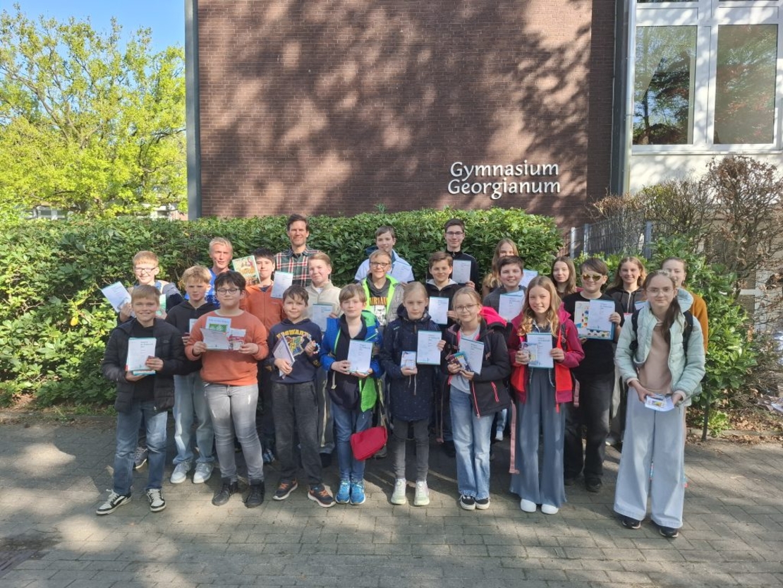Eine Sch&uuml;lergruppe posiert mit Urkunden vor dem Schulgeb&auml;ude.
