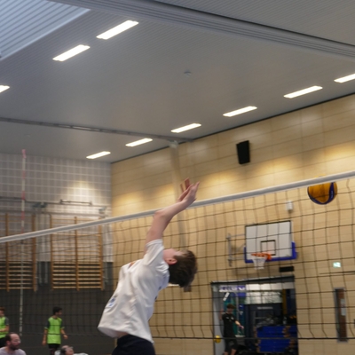 Jugendlicher schl&auml;gt einen Volleyball am Netz in einer Sporthalle.