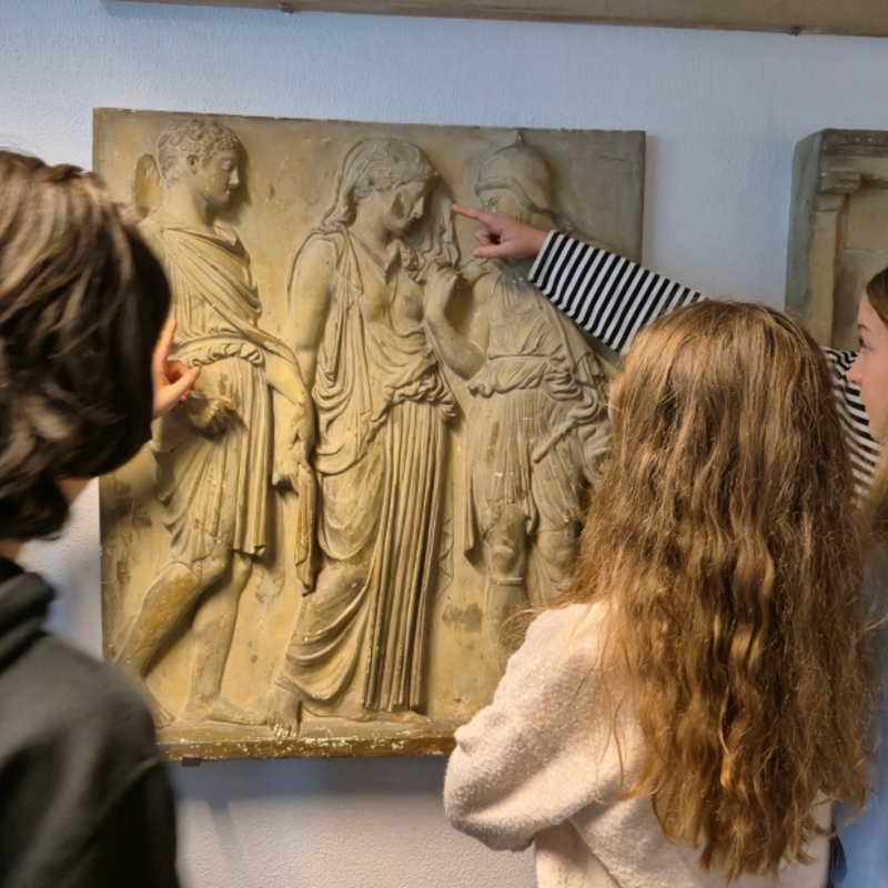 Sch&uuml;lerinnen und Sch&uuml;ler betrachten gemeinsam ein antikes Relief im Museum.