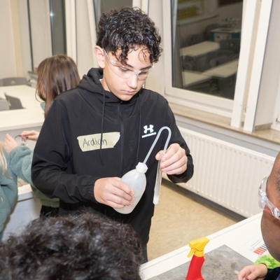 Sch&uuml;ler demonstriert an einer Mitmachstation ein Experiment mit einem kleinen Gef&auml;&szlig;.
