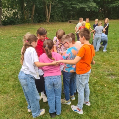 Kinder stehen im Freien eng zusammen und machen gemeinsam eine Gruppen&uuml;bung.