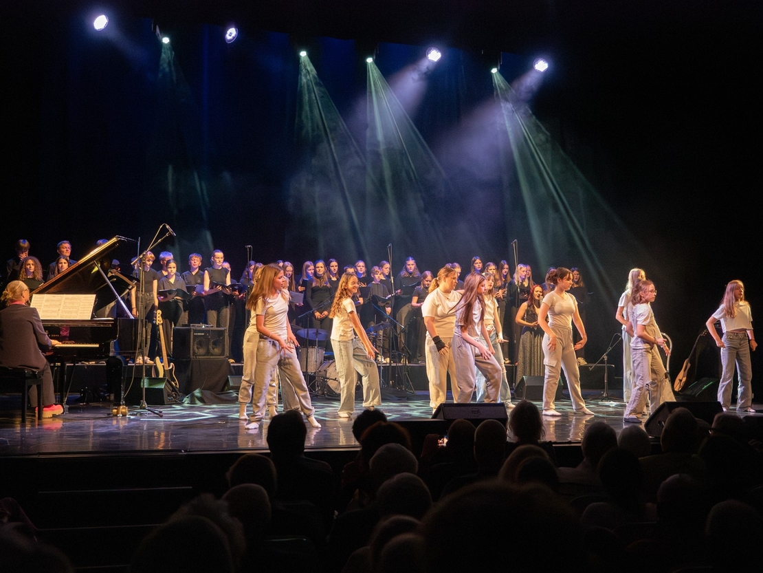 T&auml;nzerinnen treten vor Chor und Band auf einer beleuchteten B&uuml;hne auf.