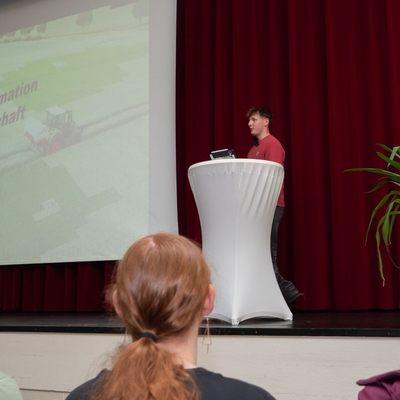 Publikum verfolgt eine Pr&auml;sentation mit projizierter Folie.