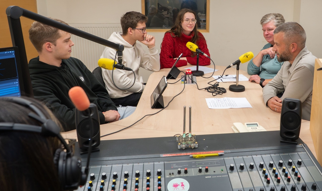 Mehrere Jugendliche und ihre erwachsenen Gespr&auml;chspartner reden bei einer Podcastaufnahme an einem Studiotisch.