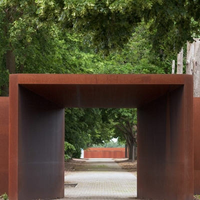 Blick durch einen rostfarbenen Stahlrahmen auf einen Weg im Gel&auml;nde der Gedenkst&auml;tte.