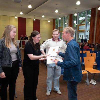 Drei Jugendliche nehmen nach ihren Vortr&auml;gen Danksagungsurkunden von einem Lehrer in Empfang.