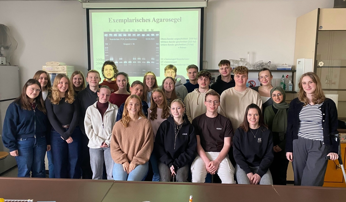 Sch&uuml;lergruppe posiert gemeinsam in einem Sch&uuml;lerlabor vor einer Pr&auml;sentationsfolie.