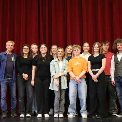Gruppe von Jugendlichen und Erwachsenen posiert gemeinsam auf einer B&uuml;hne.