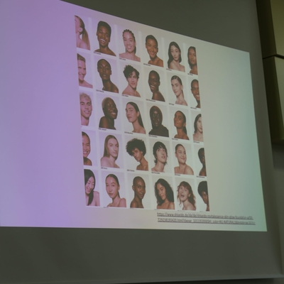 Pr&auml;sentationsfolie mit vielen Portr&auml;tbildern auf einer Leinwand.