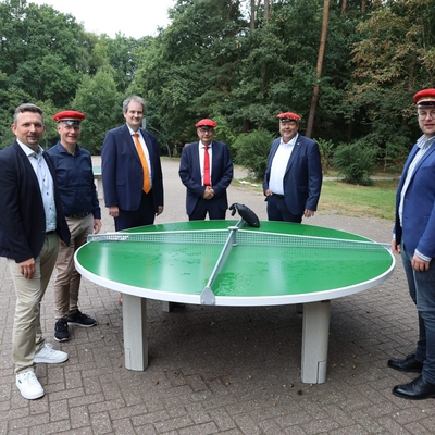 Mehrere Personen stehen im Freien um eine gro&szlig;e runde gr&uuml;ne Tischtennisplatte.