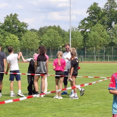 Jugendliche Sportlerinnen und Sportler besprechen sich auf einem Sportplatz.