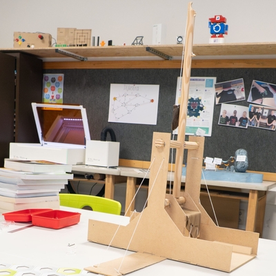 Modell eines Trebuchets aus Holz auf einem Tisch mit Werkmaterialien.