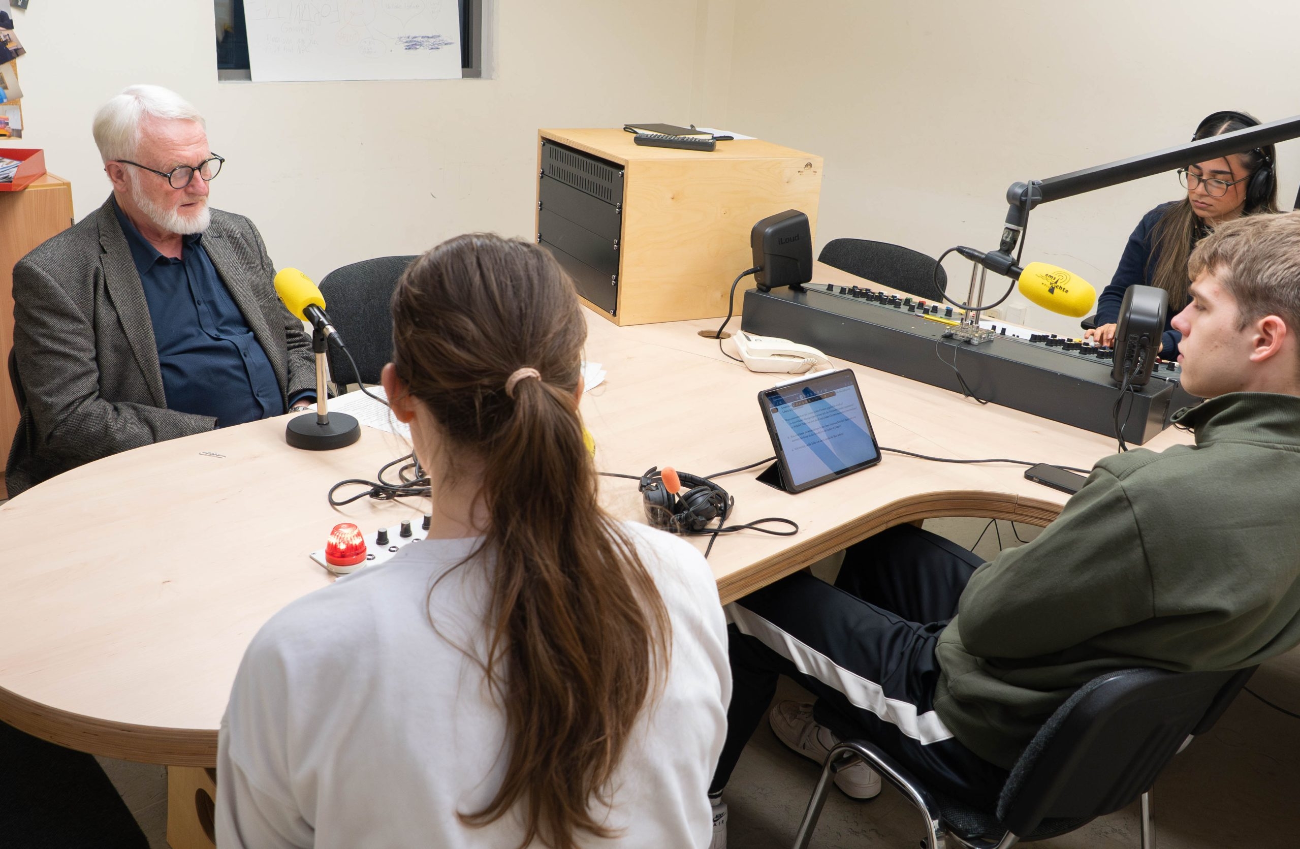 Jugendliche und ein &auml;lterer Gespr&auml;chspartner sitzen bei einer Podcastaufnahme an einem Tisch im Tonstudio.