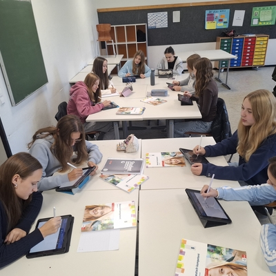 Sch&uuml;lerinnen und Sch&uuml;ler arbeiten gemeinsam an Tischen im Unterricht.