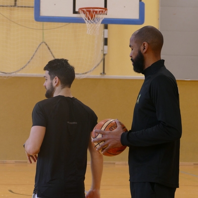 Zwei erwachsene G&auml;ste stehen mit Basketb&auml;llen in einer Sporthalle.