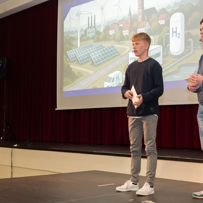 Jugendliche halten einen Vortrag auf einer B&uuml;hne vor einer projizierten Folie.