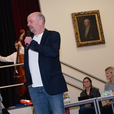 Ein Lehrer spricht auf einer B&uuml;hne in einem Veranstaltungsraum.