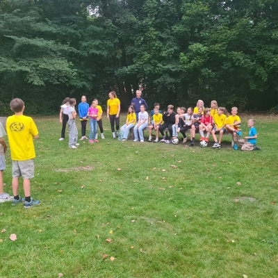 Kinder sitzen und stehen als Gruppe auf einer Wiese im Freien.