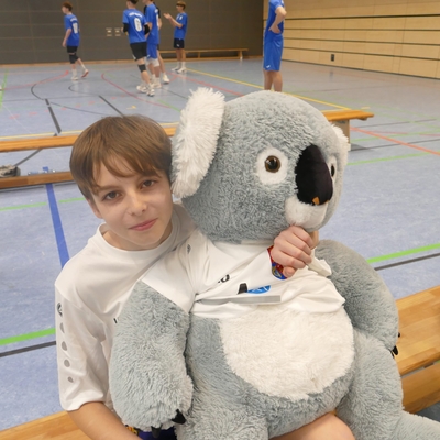 Jugendlicher sitzt mit einem Koala-Maskottchen in der Sporthalle.