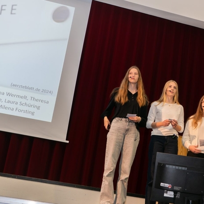 Vier Jugendliche sprechen bei einem Vortrag auf einer B&uuml;hne.