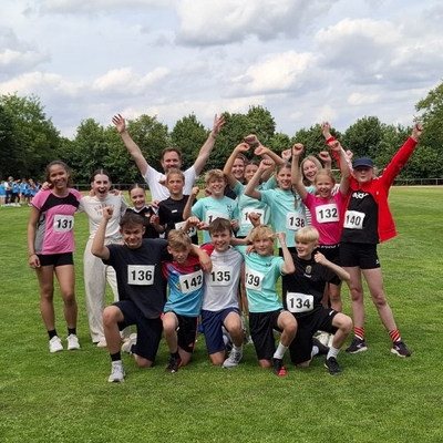 Ein Leichtathletikteam in Jubelpose auf einem Sportplatz.