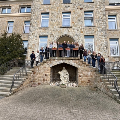 Gruppe von Sch&uuml;lerinnen und Sch&uuml;lern steht vor einem Klostergeb&auml;ude auf einer Freitreppe.