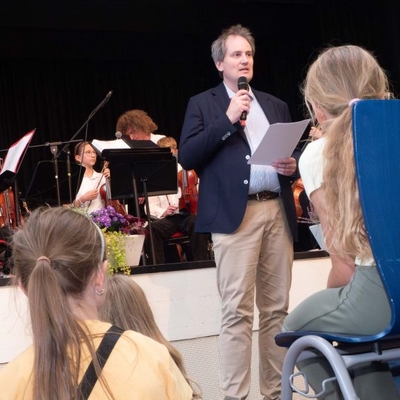 Der Schulleiter spricht vor Publikum in einem Veranstaltungsraum.