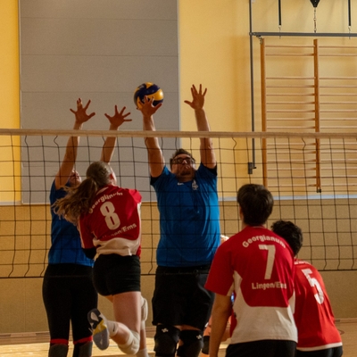 Jugendliche und Lehrkr&auml;fte springen bei einem Volleyballspiel am Netz nach dem Ball.