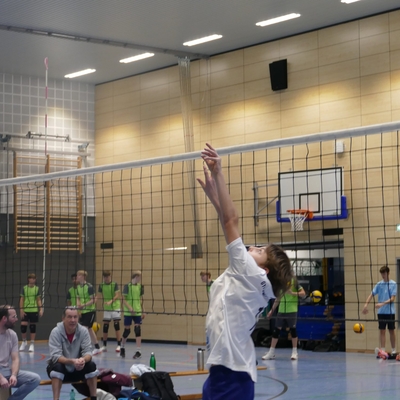 Jugendlicher springt am Netz nach dem Volleyball.