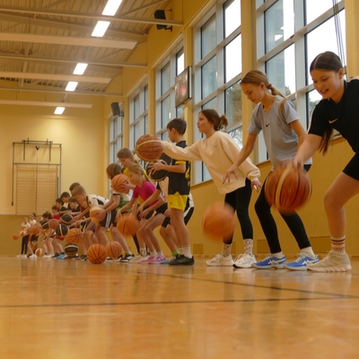 Sch&uuml;lerinnen und Sch&uuml;ler &uuml;ben in einer Reihe mit Basketb&auml;llen in der Sporthalle.