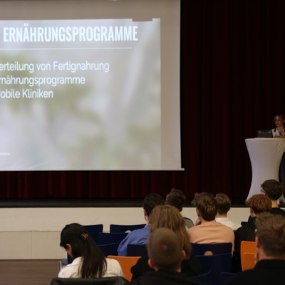 Textfolie wird auf eine Leinwand projiziert, Publikum sitzt davor.