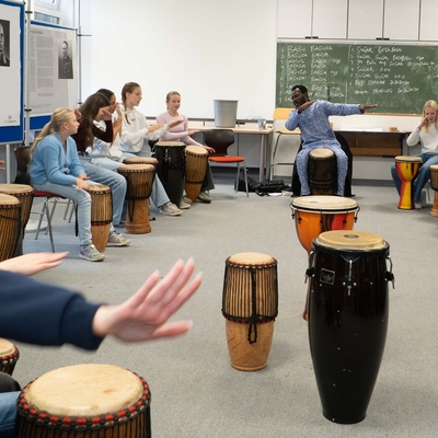 Sch&uuml;lerinnen und Sch&uuml;ler musizieren in einem Raum mit Trommeln.