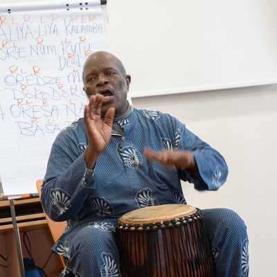 Ein Mann sitzt vor einer Trommel und erkl&auml;rt den Teilnehmenden einen Rhythmus.