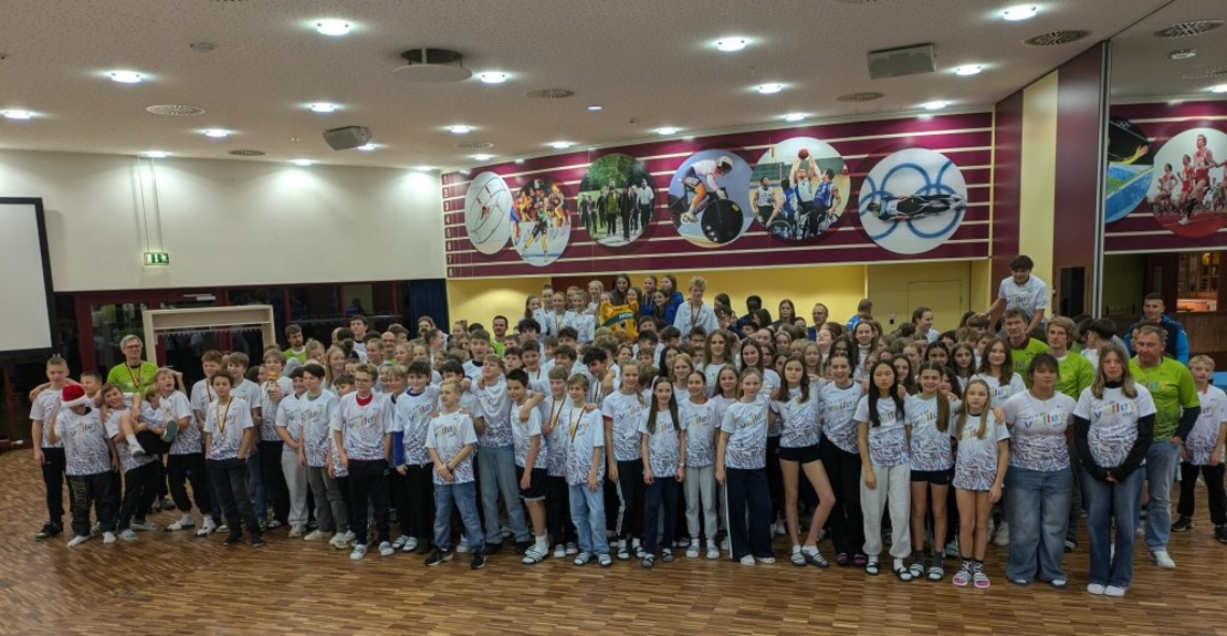 Gro&szlig;e Gruppe von Sch&uuml;lerinnen, Sch&uuml;lern und Begleitpersonen posiert gemeinsam in einer Halle.