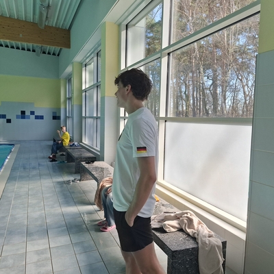 Jugendlicher steht am Beckenrand eines Hallenbads.