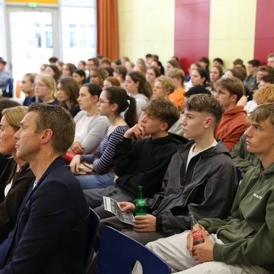 Publikum sitzt in Reihen und verfolgt eine Pr&auml;sentation.