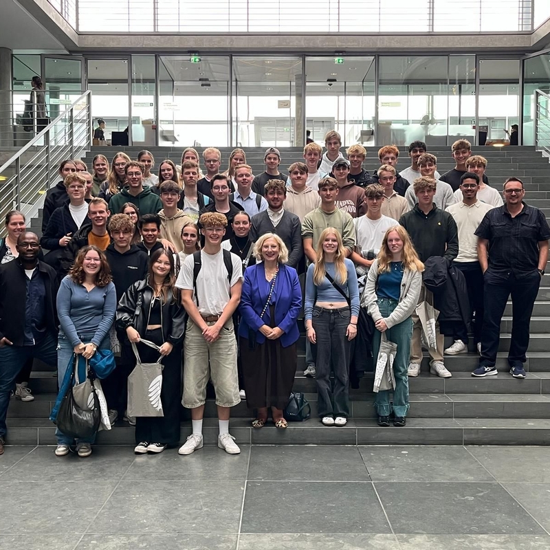Sch&uuml;lergruppe mit Lehrkr&auml;ften posiert auf einer Treppe in einem Geb&auml;ude.