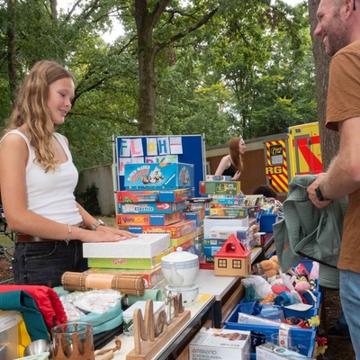 Eine Sch&uuml;lerin und ein Erwachsener im Gespr&auml;ch an einem Flohmarktstand.