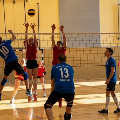 Mehrere Jugendliche springen in einer Sporthalle am Netz nach dem Ball.