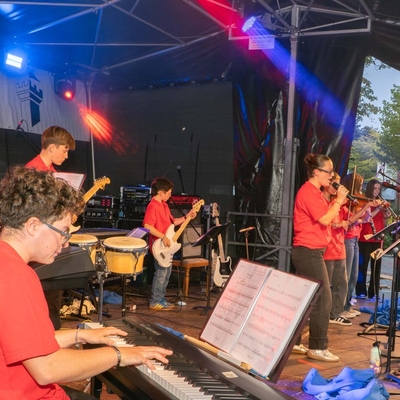Jugendliche Musiker treten auf einer beleuchteten Au&szlig;enb&uuml;hne auf.