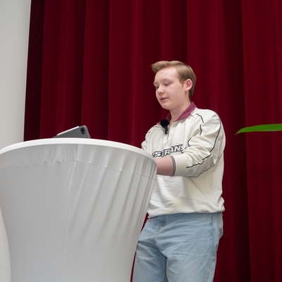 Ein Jugendlicher h&auml;lt einen Vortrag an einem Stehtisch auf der B&uuml;hne.