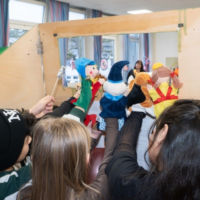 Kinder schauen einer bunten Puppentheater-Szene in einem Klassenraum zu.