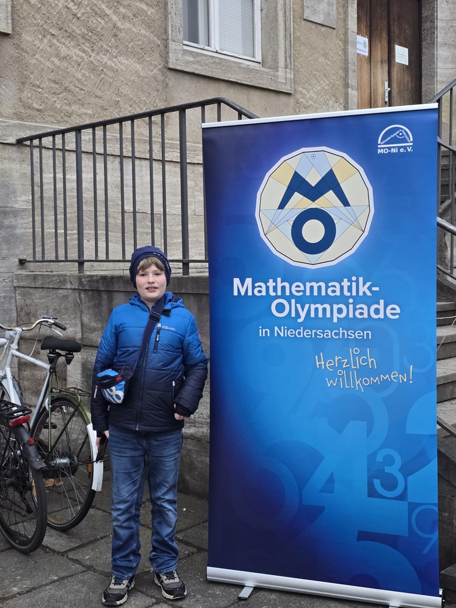 Ein Sch&uuml;ler posiert vor einem Plakat der Mathematik-Olympiade in Niedersachsen.