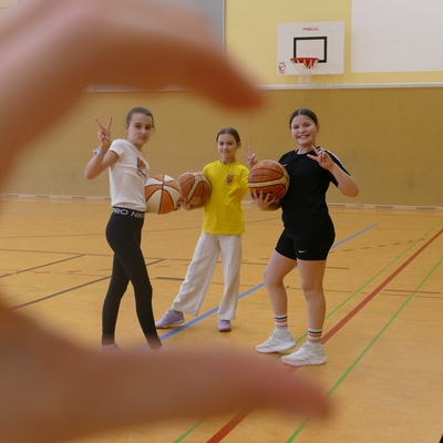 Drei Sch&uuml;lerinnen stehen mit Basketb&auml;llen in einer Sporthalle.