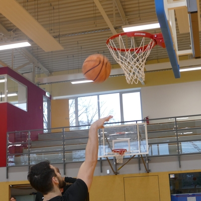 Jugendlicher wirft einen Basketball in Richtung Korb in einer Sporthalle.