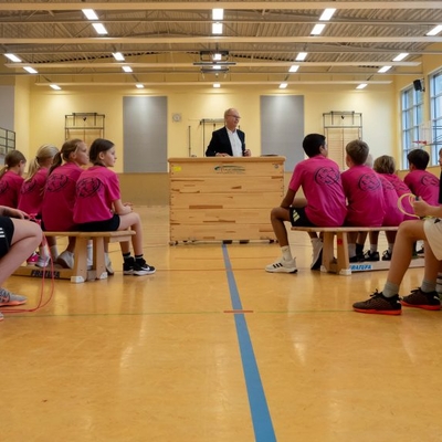 Kinder sitzen in einer Sporthalle und schauen nach vorn zu einer Ehrung oder Ansprache.