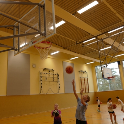 Jugendliche spielen Basketball unter einem Korb in der Sporthalle.