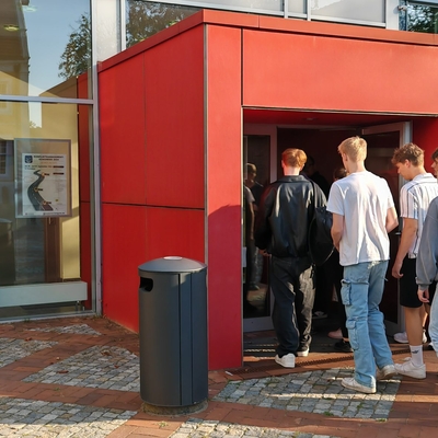 Mehrere Jugendliche betreten einen roten Geb&auml;udeeingang.