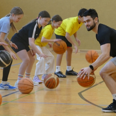 Jugendliche &uuml;ben gemeinsam mit einem erwachsenen Trainer das Dribbeln in einer Sporthalle.